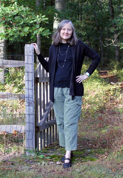 Lee Ann Thill, standing at an open gate with woods behind her
